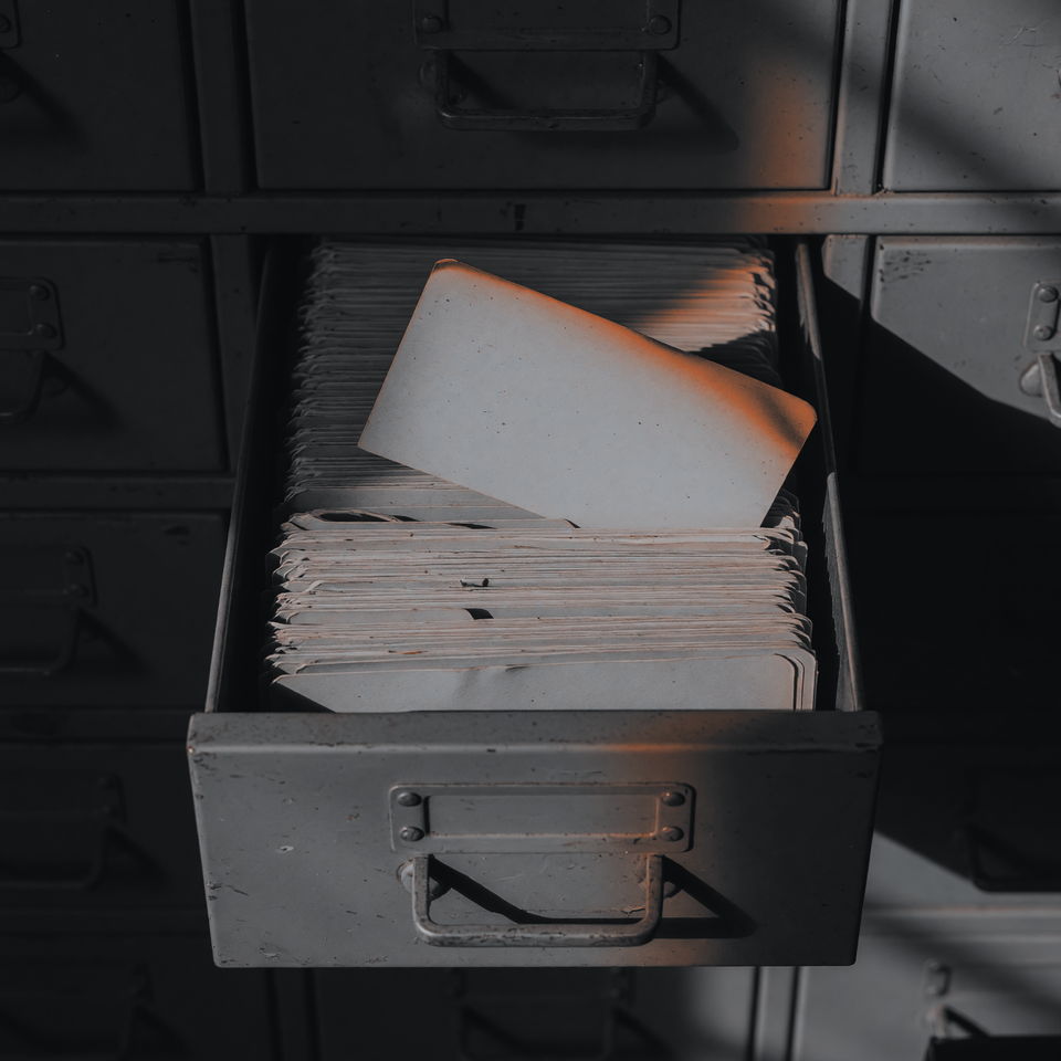 An open metal filing drawer packed with index cards, one card standing higher than the rest, lit from the side.